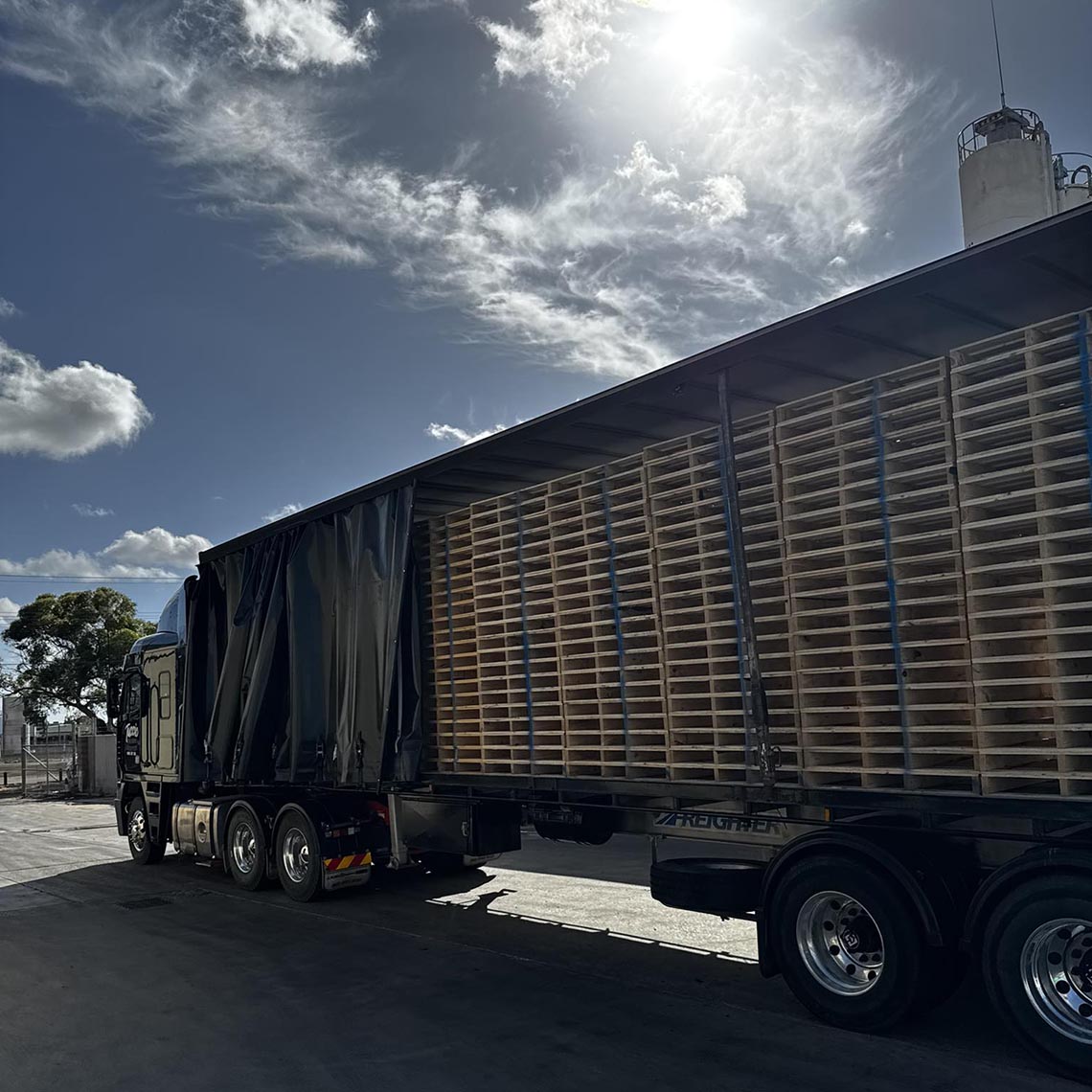 Curtain-sider semi-trailer with its curtains open, loaded with timber pallets